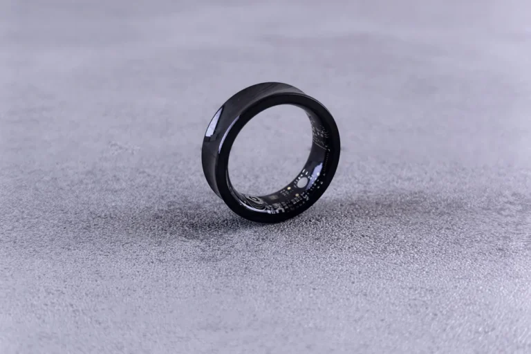 A black smart ring standing on its edge on a lilac-grey textured surface