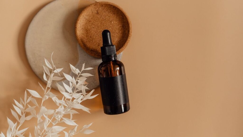 An amber dropper bottle with dried white flowers and a cork tray on a warm beige background