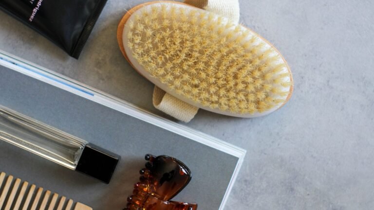A natural-bristle hairbrush, a wooden comb and hair-care tubes laid out on grey stone