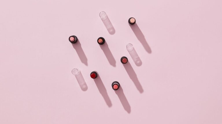 Several uncapped lipsticks in different shades casting long shadows on a pink surface