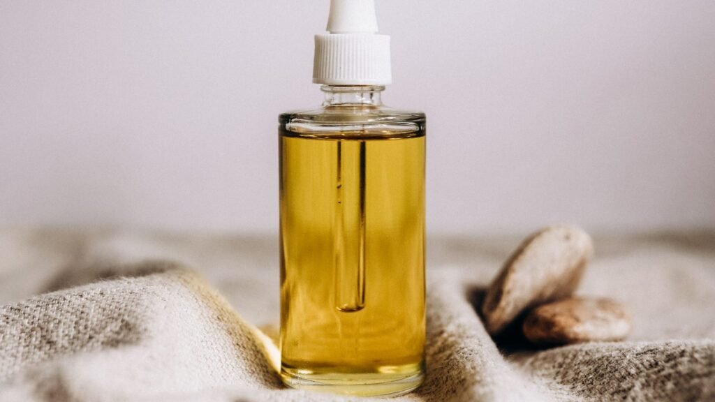 A clear glass dropper bottle of golden facial oil resting on soft beige woven fabric
