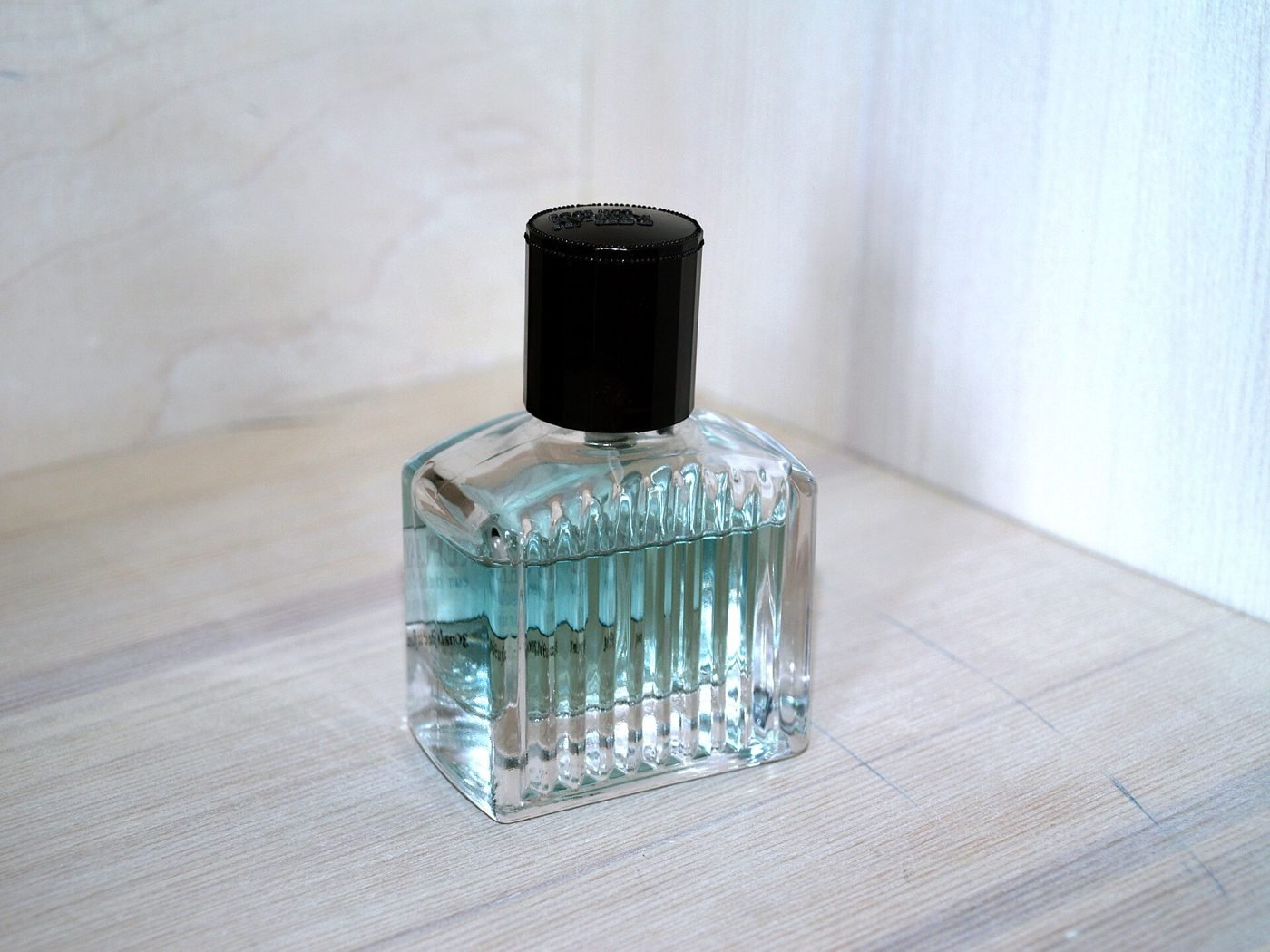 A glass perfume bottle with a black cap on a white surface