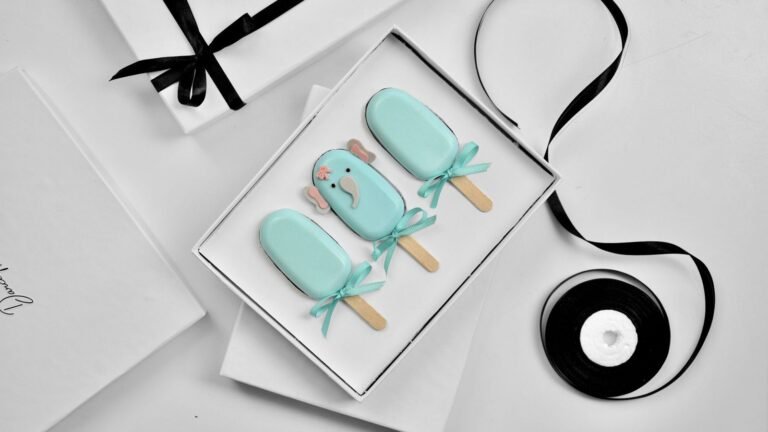 Handmade popsicle-shaped soaps in an open white gift box beside a black satin ribbon
